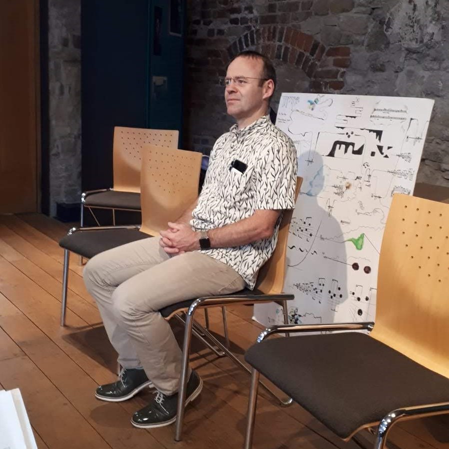 Sean Roe engaged by a performance, sitting beside a giant graphic score